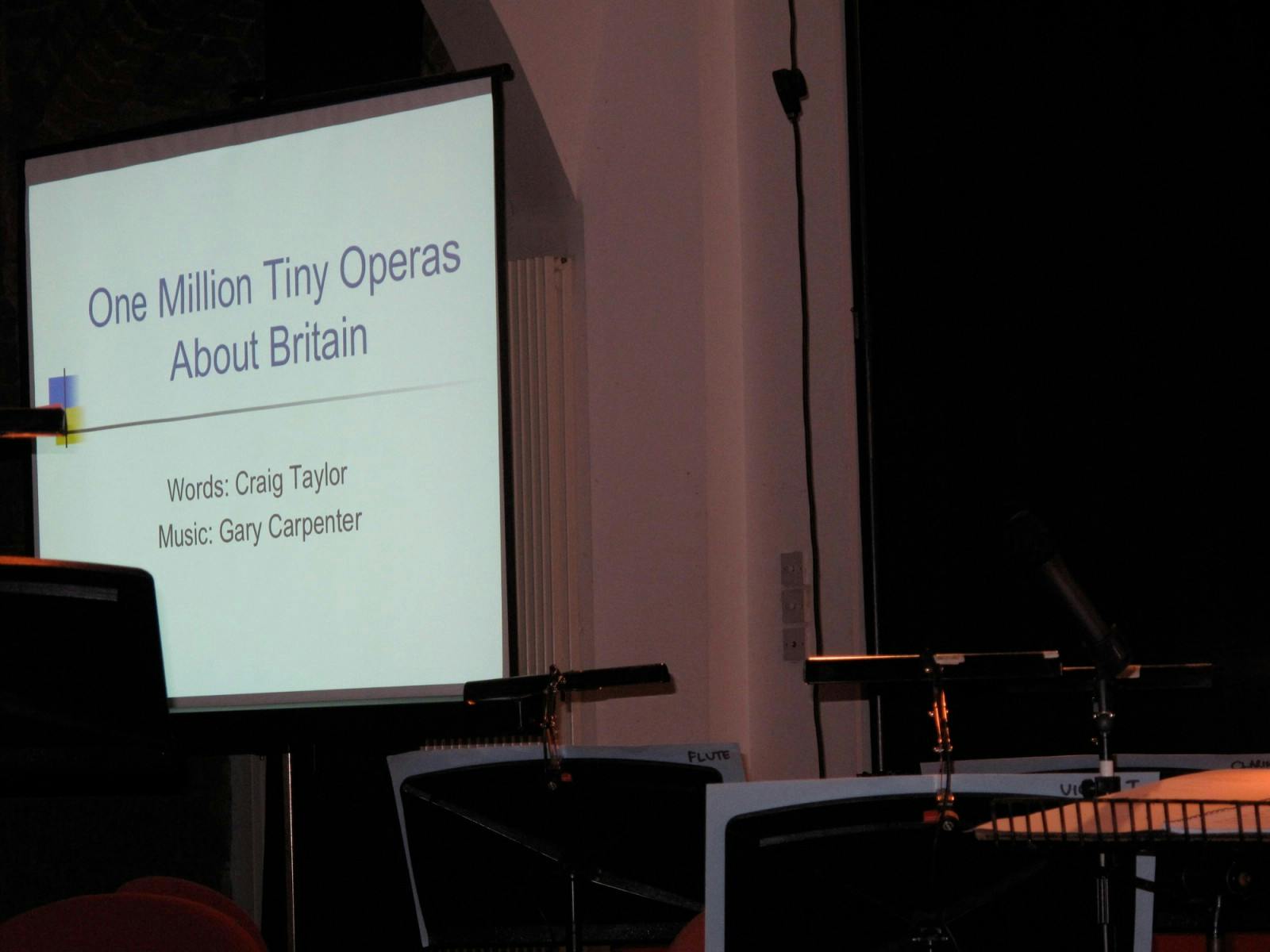A projector screen with the text "One Million Tiny Operas About Britain"